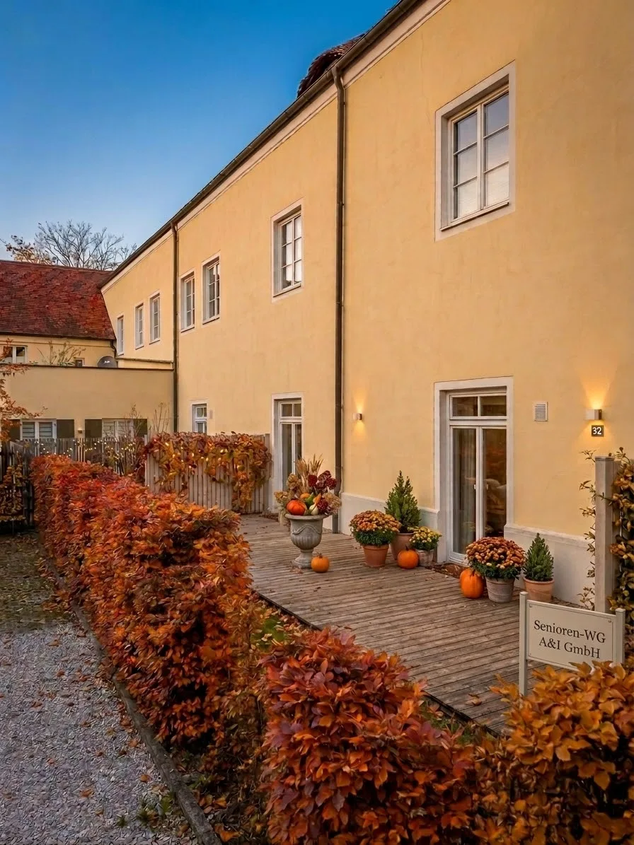 Außenansicht des Hauses der Senioren-WG mit Holzterrasse, Herbstpflanzen und dem Schild „Senioren-WG A&I GmbH“.